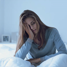 Een persoon zit vermoeid op bed.