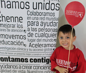 Kind met rood Duchenne t-shirt en ballon bij een banner.