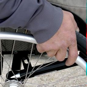 Een hand aan het wiel van een rolstoel.