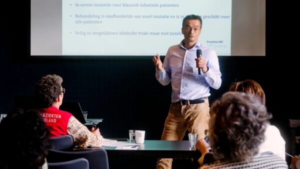 Een medisch specialist geeft een lezing aan mensen in een zaal op een bijeenkomst van Spierziekten Nederland.